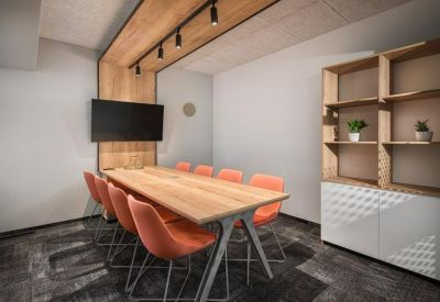 Modern meeting room featuring an light wood table, orange chairs, and a wall-mounted TV.