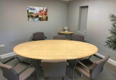 Boardroom featuring an oval wooden table and grey upholstered chairs.