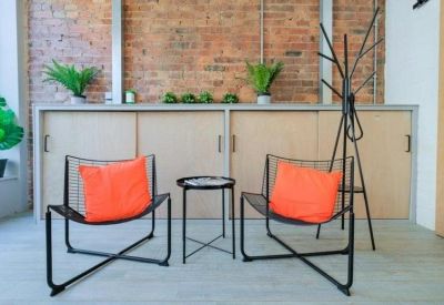 Communal breakout area with stylish black wire chairs, orange cushions, and an exposed brick wall.
