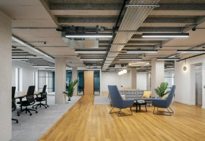 Bright open-plan office featuring blue lounge chairs, wooden floors, and exposed ceiling details.