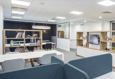 Open-plan coworking space with long white desks and wooden partition shelving.