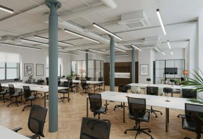 Spacious open-plan office with white desks, ergonomic black chairs, and industrial-style grey pillars.