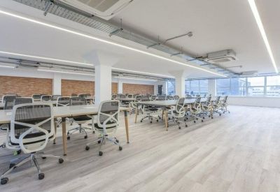 Open-plan office space with rows of ergonomic chairs and long white desks.