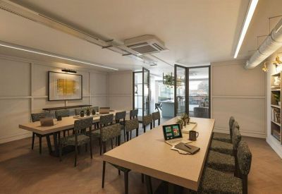 Light-filled meeting room with a large wooden table, green chairs, and a glass partition.