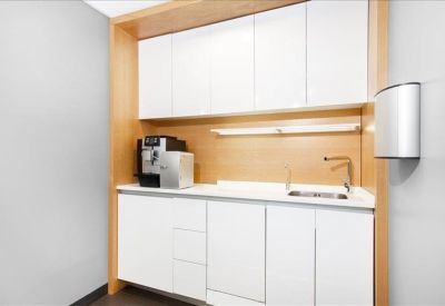 Sleek office kitchenette with white cabinetry and wooden accents.