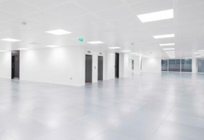 Spacious, empty open-plan office floor with bright overhead lighting and white walls.