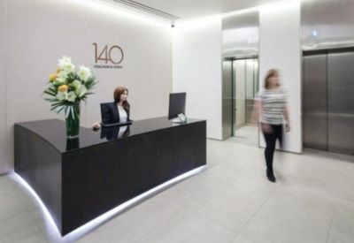 Modern reception area with a black L-shaped desk, floral arrangement, and nearby elevators.