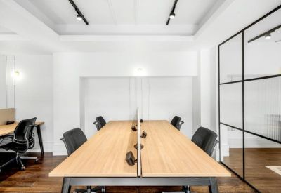 Modern open-plan office desks with black ergonomic chairs and a glass wall.
