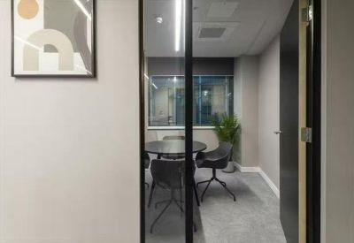 Small private meeting room with a round table and grey chairs behind a glass partition.