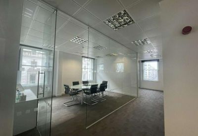 Glass-walled meeting room with a central table and black office chairs.