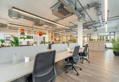 Bright open-plan workspace with white desks, ergonomic black chairs, and exposed ceiling ductwork.