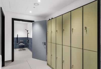 Bright hallway featuring a row of olive-green lockers and a doorway leading to a blue-tiled room.