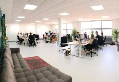 Spacious open-plan office with white desks, ergonomic chairs, and large windows.