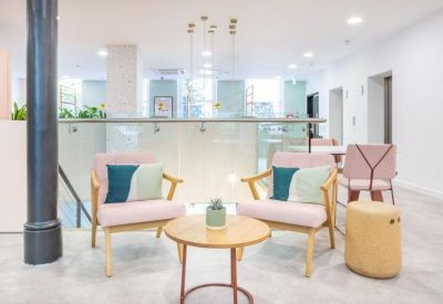 Bright communal lounge area featuring pink armchairs and a glass mezzanine railing.