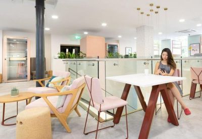 Spacious coworking area with pink chairs, wooden tables, and a large black support pillar.