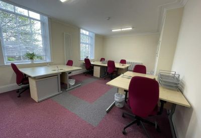 Spacious shared office with multiple desks, red chairs, and large windows.