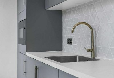 Modern kitchenette corner featuring a gold arched faucet and geometric tile backsplash.