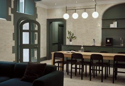 Modern communal kitchen and dining area with a long wooden table and globe pendant lights.