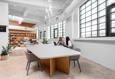 Spacious communal lounge with a large wooden table, grey chairs, and a bookshelf in the background.