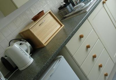 Compact communal kitchen area with wood-style cabinets and a kettle.