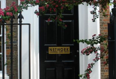 Black paneled entrance door framed by white masonry and blooming trees.
