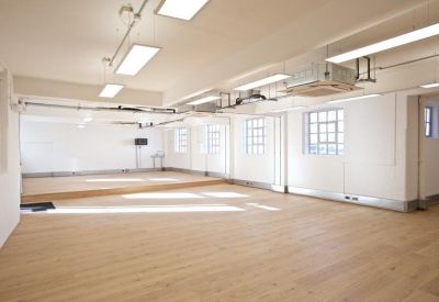 Spacious open-plan studio with light wood flooring and overhead industrial ducting.