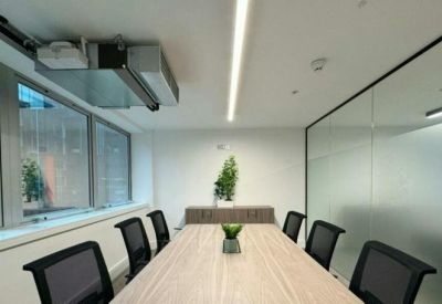 Modern meeting room with a light wood table, black chairs, and a large frosted glass partition.