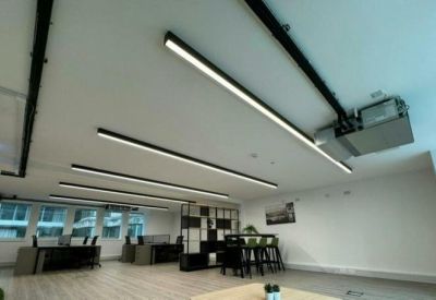 Open workspace showing rows of desks, industrial-style ceiling beams, and large windows.