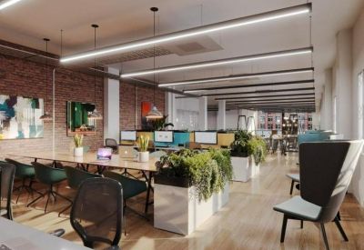 Spacious open-plan workspace featuring long wooden desks, green plants, and warm overhead lighting.