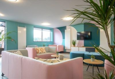 Modern breakout area featuring pink and teal seating and a large TV screen.