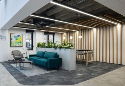 Breakout lounge with a teal sofa, wooden wall slats, and potted plants under industrial-style lighting.