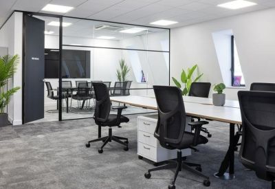 Open-plan office with white desks, ergonomic black chairs, and a glass-walled meeting room.