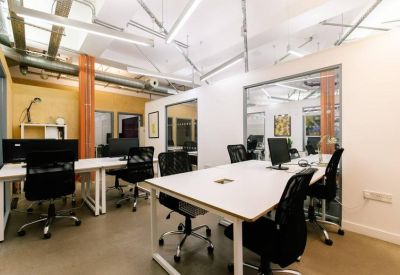 Modern shared office space featuring white desks, ergonomic black chairs, and glass partitions.