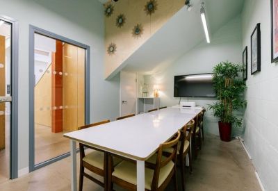 Intimate meeting room with a white table, wooden chairs, and a large wall-mounted screen.