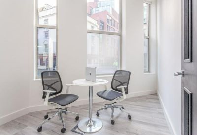 Small private office with two mesh chairs and a round white pedestal table by a window.