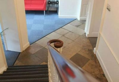 Entrance hall featuring a classic staircase with a dark wood banister and a red sofa in the background.