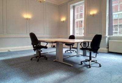 Spacious corner office with wall paneling and three black ergonomic chairs around a large desk.