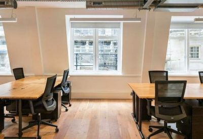 Open-plan workspace with multiple desks, black mesh chairs and hardwood flooring.