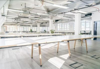 Expansive open-plan office with long white desks and industrial-style ceiling fixtures.