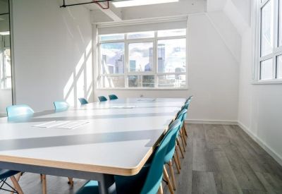 Professional meeting room with a long white table, turquoise chairs, and large windows.