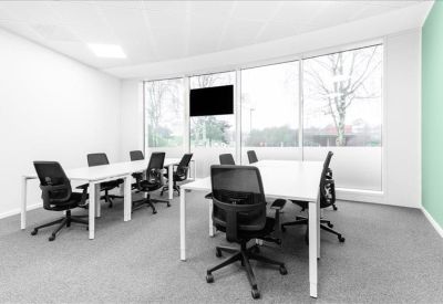 Bright open-plan coworking space with white desks and large windows.