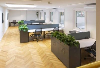 Open-plan workspace with chevron wood flooring, white desks, and lush green plants.
