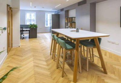 Bright communal break area with a high white table and teal velvet bar stools.