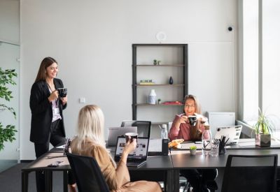 Colleagues having coffee at a shared desk in a bright, modern office space.