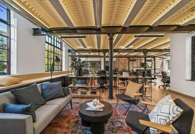 Lounge area with grey sofa, colorful rug, and exposed industrial ceiling.