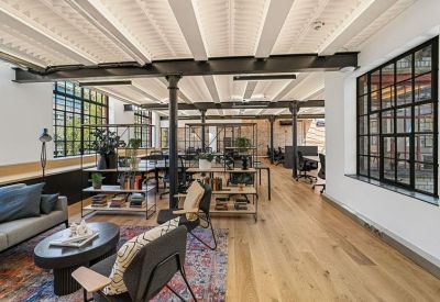 Spacious open-plan workspace with wooden floors and rows of black desks.