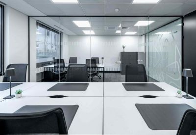 Open-plan office desks with black mesh chairs and glass partitions.