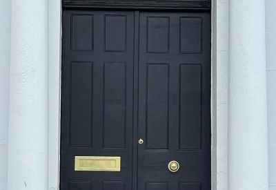 Close-up of a navy blue double entrance door with brass fixtures and white columns.