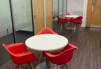 Communal breakout area with vibrant red chairs and circular white tables.