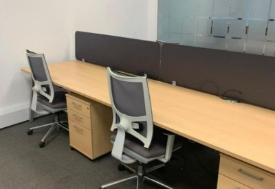 Modern office workspace with light wood desks, grey mesh chairs, and privacy dividers.